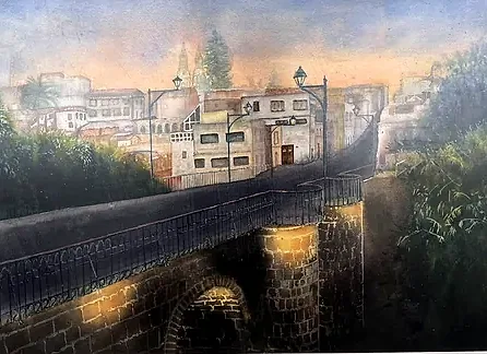 Puente de sillar con farolas encendidas al anochecer; al fondo las casas del barrio bajan hacia el río y el cielo pasa del naranja al azul.